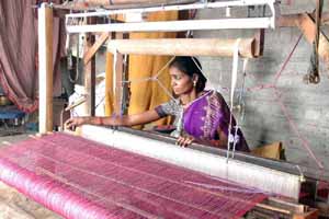 The rolled up warp is attached to the pit loom and a Self Help Group member begins weaving.